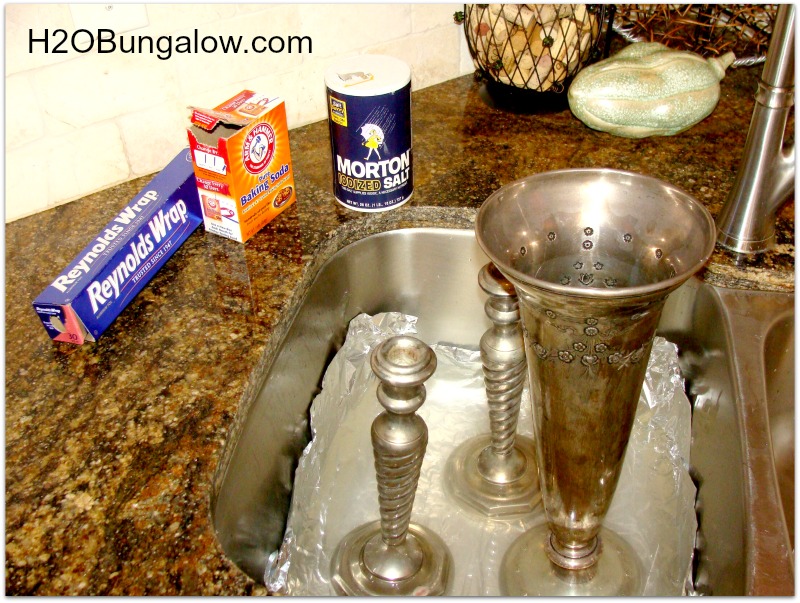 tarnished silver vase and candle sticks sitting in sink  with salt, baking soda and aluminum foil containers sitting on the counter