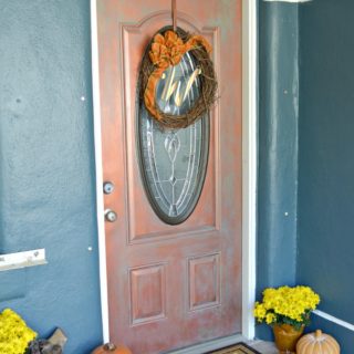 Copper front door with pumpkins on the ground on either side with a monogramed welcome mat