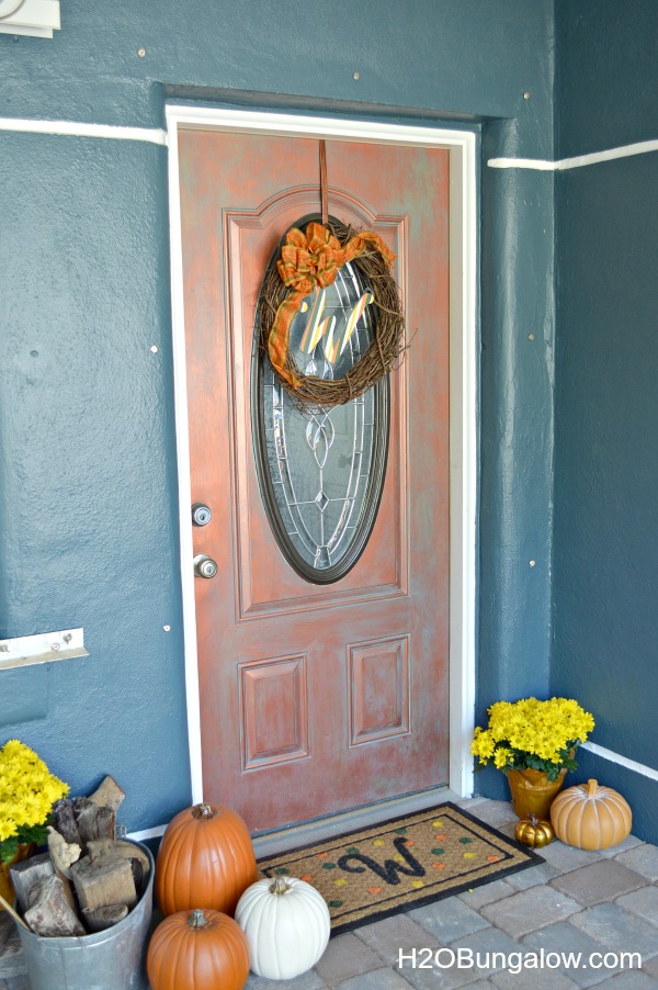 Copper front door with pumpkins on the ground on either side with a monogramed welcome mat