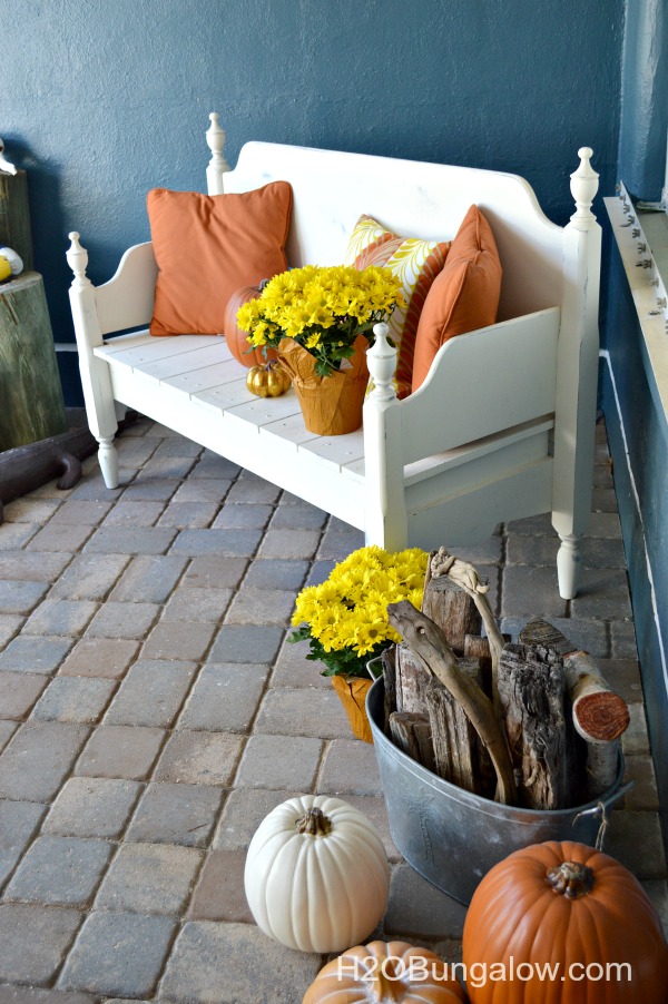 white bench made from headboard and footboard with orange pillows and yellow mums on brick patio