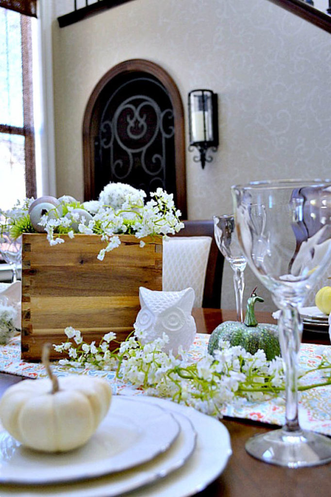 White plates with a small pumpkin sitting on with an owl in the centerpiece on a Thanksgiving tablescape