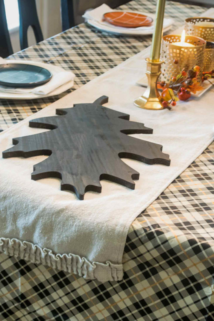 Large wooden leaf shaped tray on a table runner sitting on a plaid tablecloth