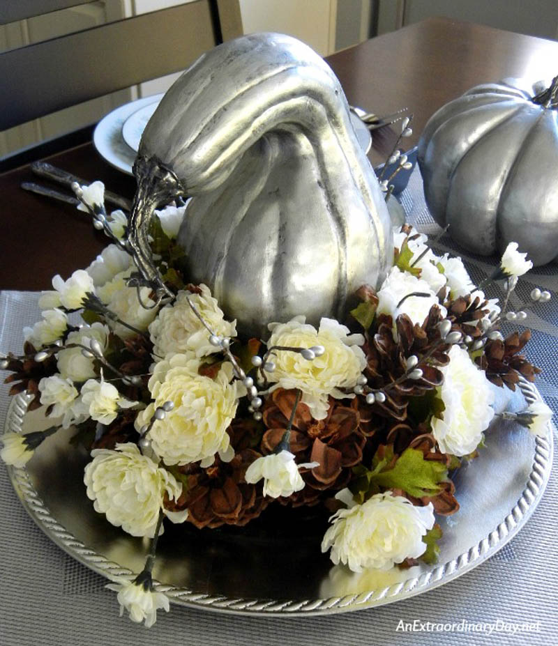 Gourds painted silver sitting in the middle of a flower arrangement