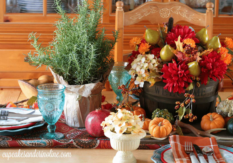 Colorful tablescape with red and orange flowers, pumpkins and  mini evergreen in a burlap sack