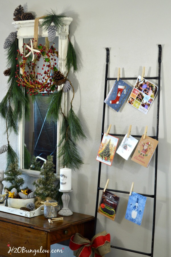 My festive holiday entry makes good use of an entry table in a tight space to stage a warm welcome with a multi-purpose vignette, Christmas cards hang nicely on the metal ladder and a bucket of lap blankets are perfect for a chilly night add to a pretty entry with simple decor. www.H2OBungalow.com #Smallspace 