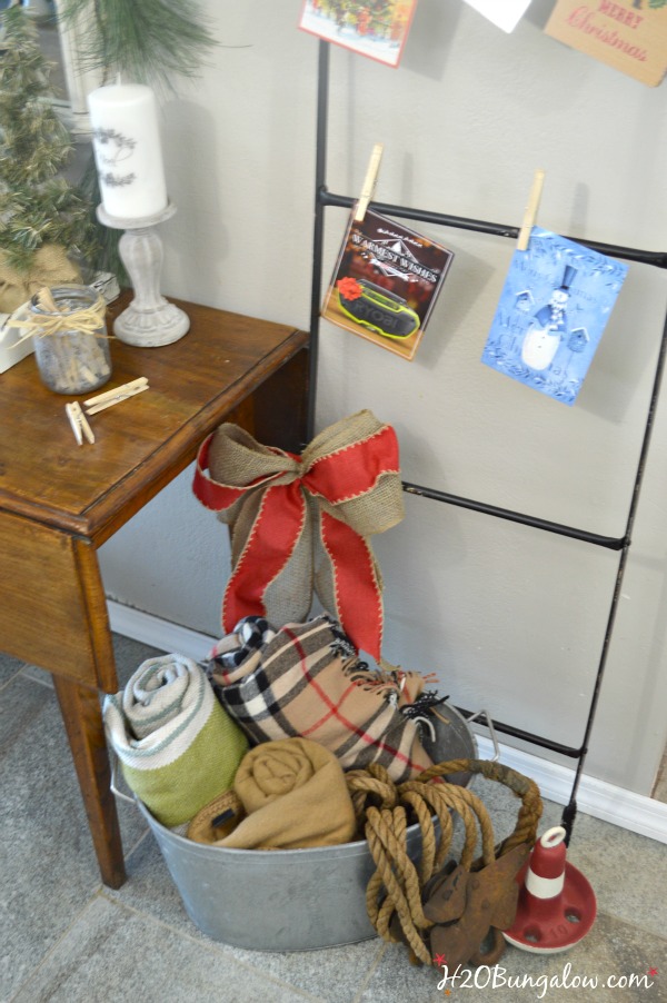 My festive holiday entry makes good use of an entry table in a tight space to stage a warm welcome with a multi-purpose vignette, Christmas cards hang nicely on the metal ladder and a bucket of lap blankets are perfect for a chilly night add to a pretty entry with simple decor. www.H2OBungalow.com #Smallspace 