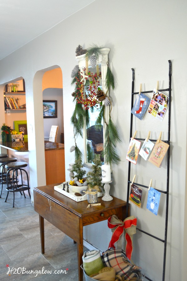 My festive holiday entry makes good use of an entry table in a tight space to stage a warm welcome with a multi-purpose vignette, Christmas cards hang nicely on the metal ladder and a bucket of lap blankets are perfect for a chilly night add to a pretty entry with simple decor. www.H2OBungalow.com #Smallspace 