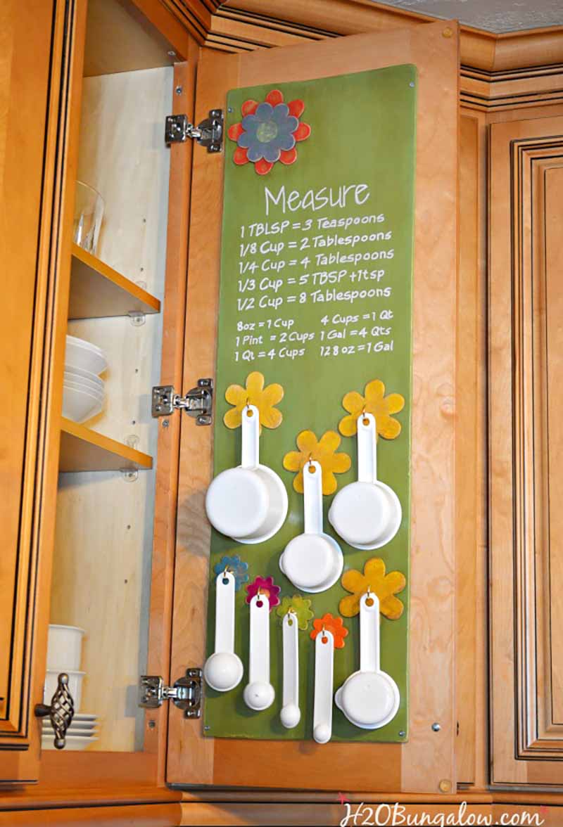 white measuring cups and spoons hanging on the inside of cabinet door, one of the best kitchen organizing ideas