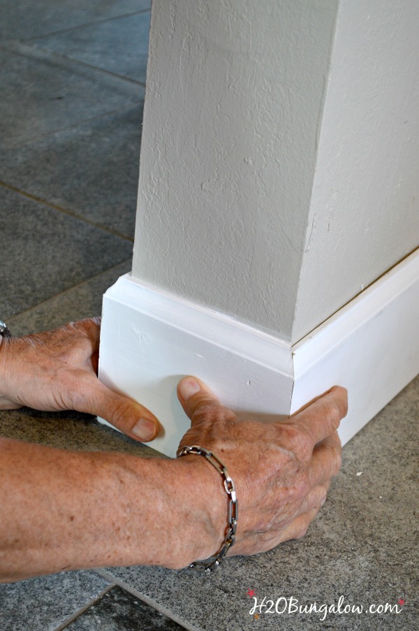 DIY baseboard tutorial shown being installed with two hands holding it.