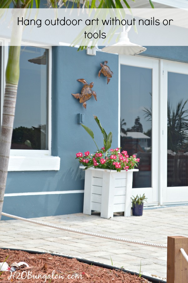 outdoor of blue house shown with white planter with pink flowers and turtles hung on house. 