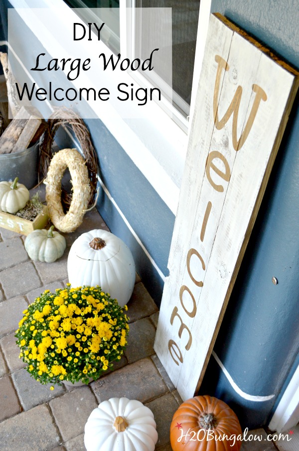 Large wood welcome sign on the porch with pumpkins and yellow mums.