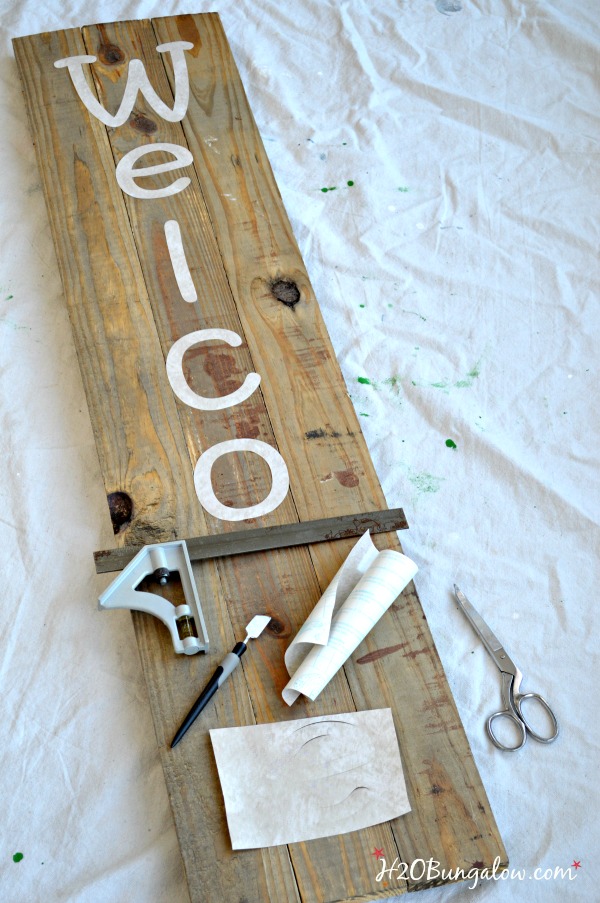 Stencil letters spelling Welcome laying on wood with tools.