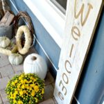 Large wood welcome sign on the front porch with pumpkins and yellow mums