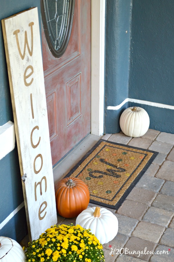 Large wood welcome sign on the front porch with pumpkins and yellow mums