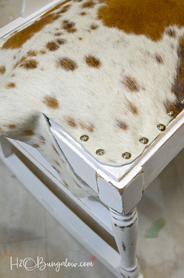 Tutorial and tips to make a DIY nailhead trimmed cowhide seat. Take an old wood seat on a bench or chair and transform it to an upscale and trendy cowhide piece of home decor. Depending on the piece you use it will look great in a farmhouse or modern home! 