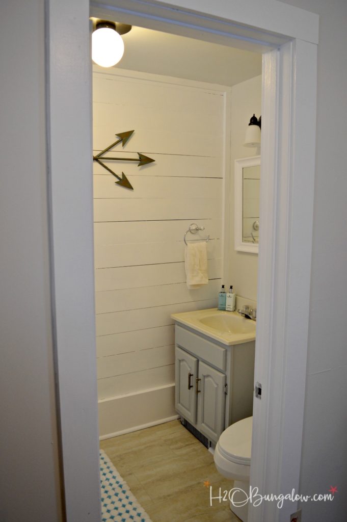 completed bathroom with shiplap walls white mirror and bronze light fixture