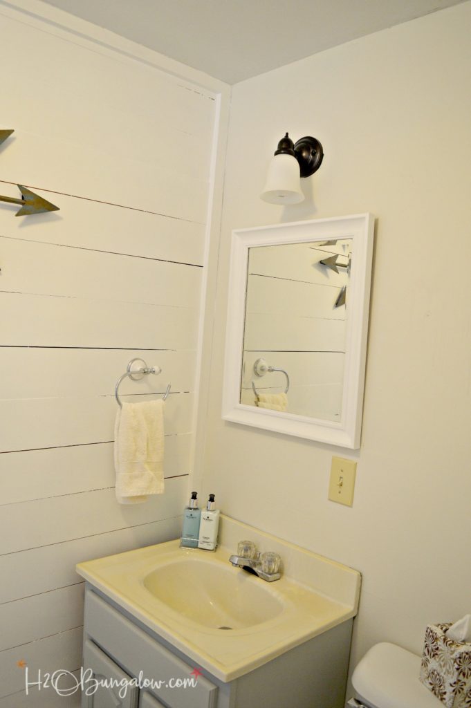 completed bathroom with shiplap walls white mirror and bronze light fixture