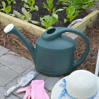 watering can, hat and gloves sitting on ground next to the DIY raised garden bed