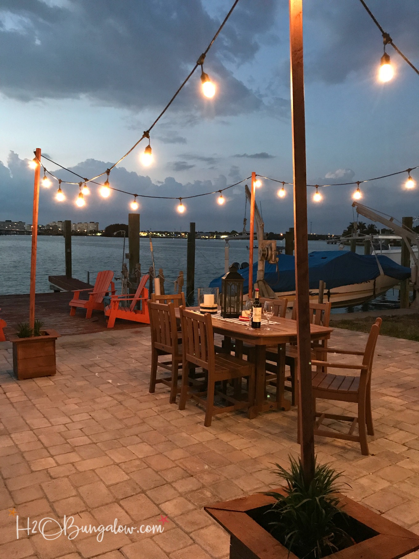 DIY outdoor string lights on poles shown at night on patio with wood table and chairs.