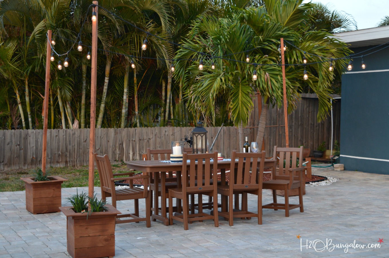DIY outdoor string lights on poles shown on patio with wood patio table and chairs