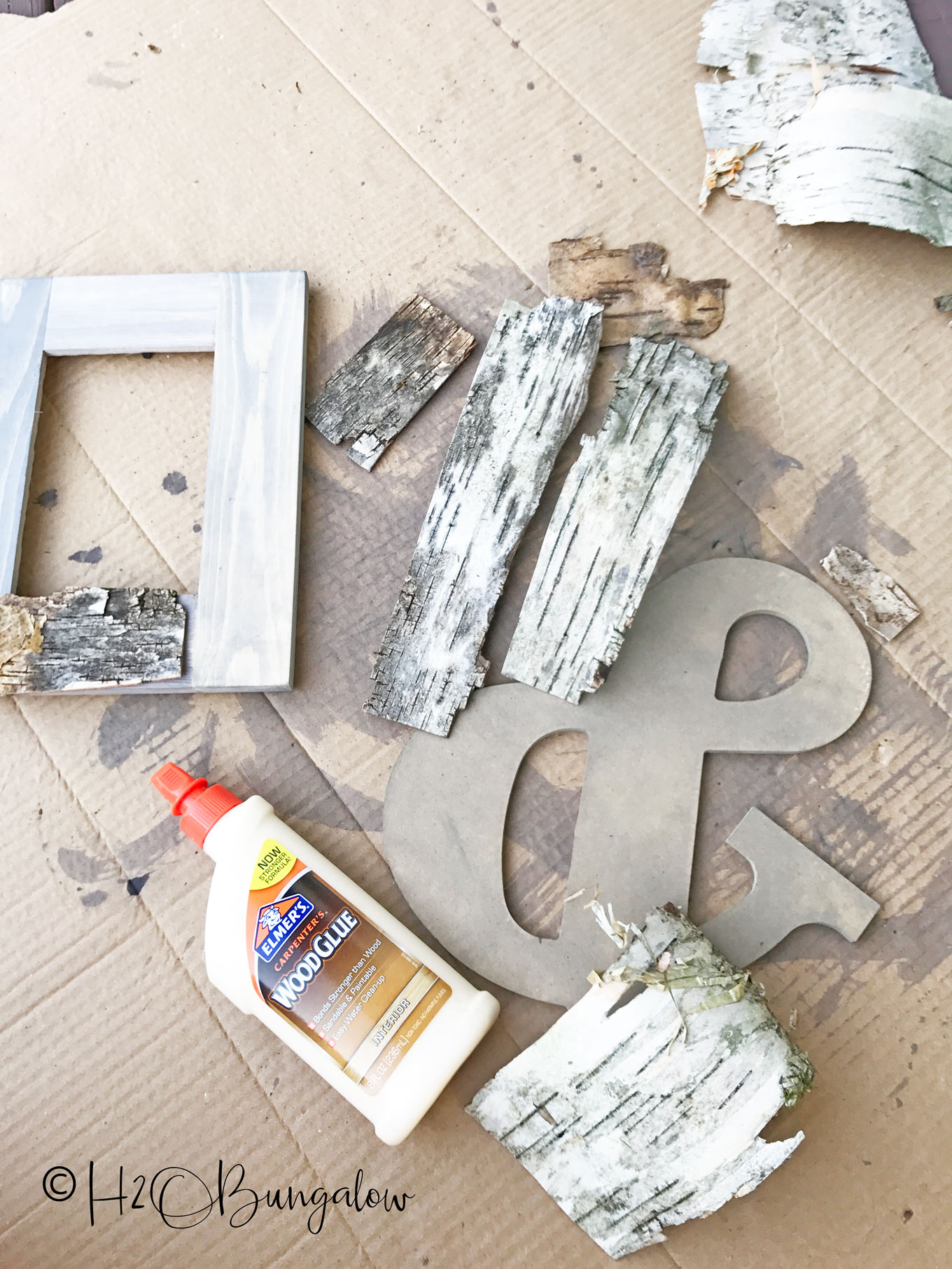 birch bark pieces, wood glue, frame, and ampersand sitting on cardboard