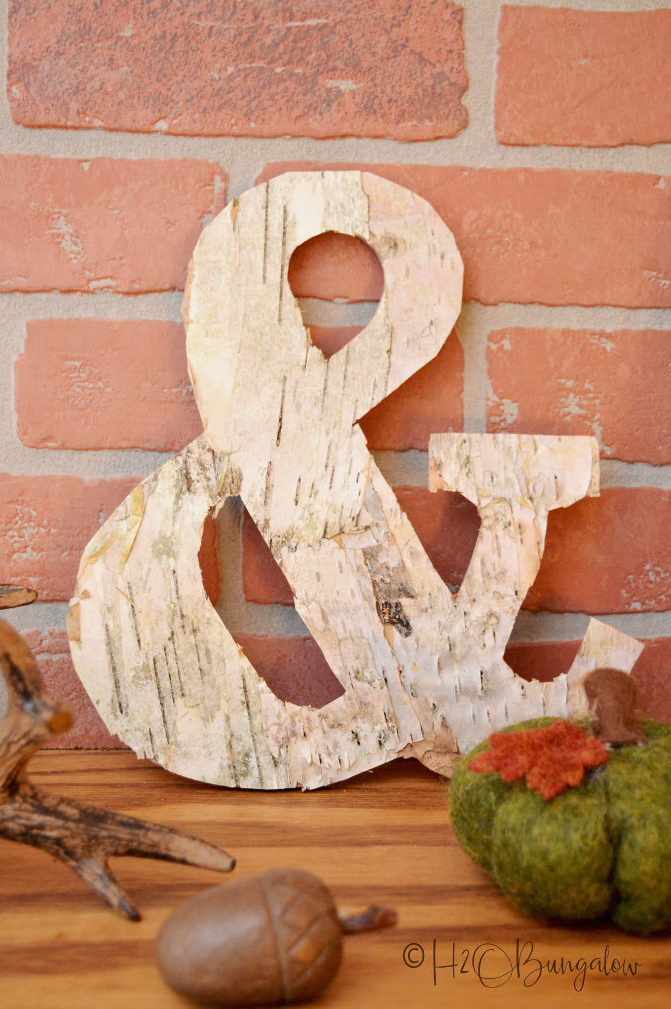 Ampersand covered with birch bark sitting on mantle with green fabric pumpkin