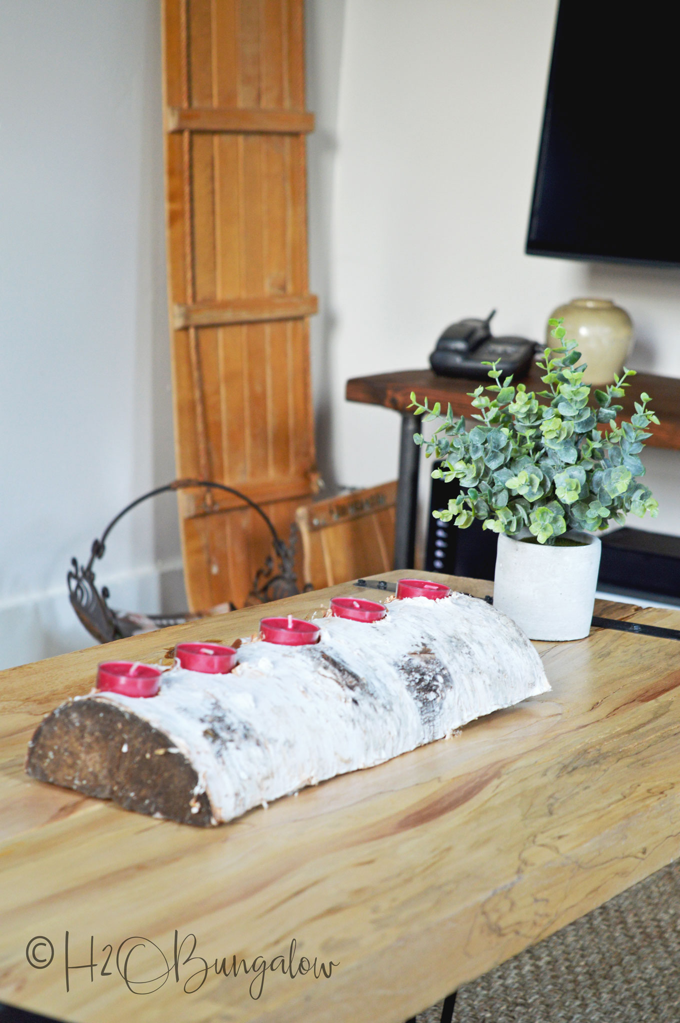 Birch log candle holder with five red tea lights sitting on wood coffee table