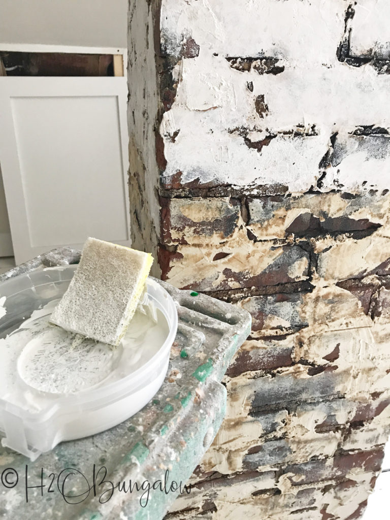 brick with plaster on it with sponge and paint tray on a ladder