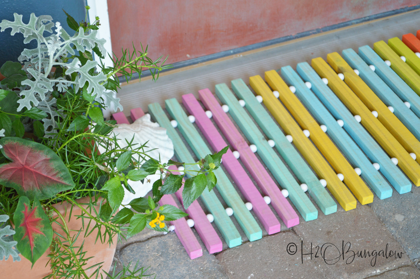 spring outdoor DIY project using 1x1 boards to make a colorful wood slat door mat painted pink, green, yellow, and blue.