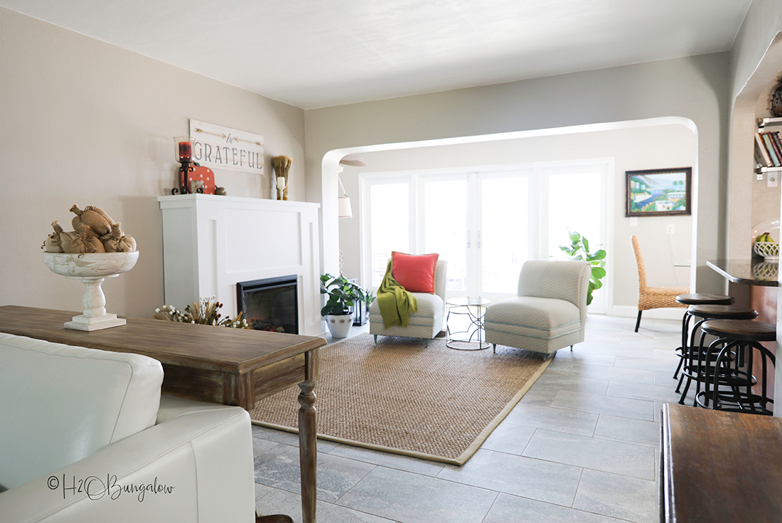 Beautiful living room with DIY fireplace shown with beige rug and two white chairs.