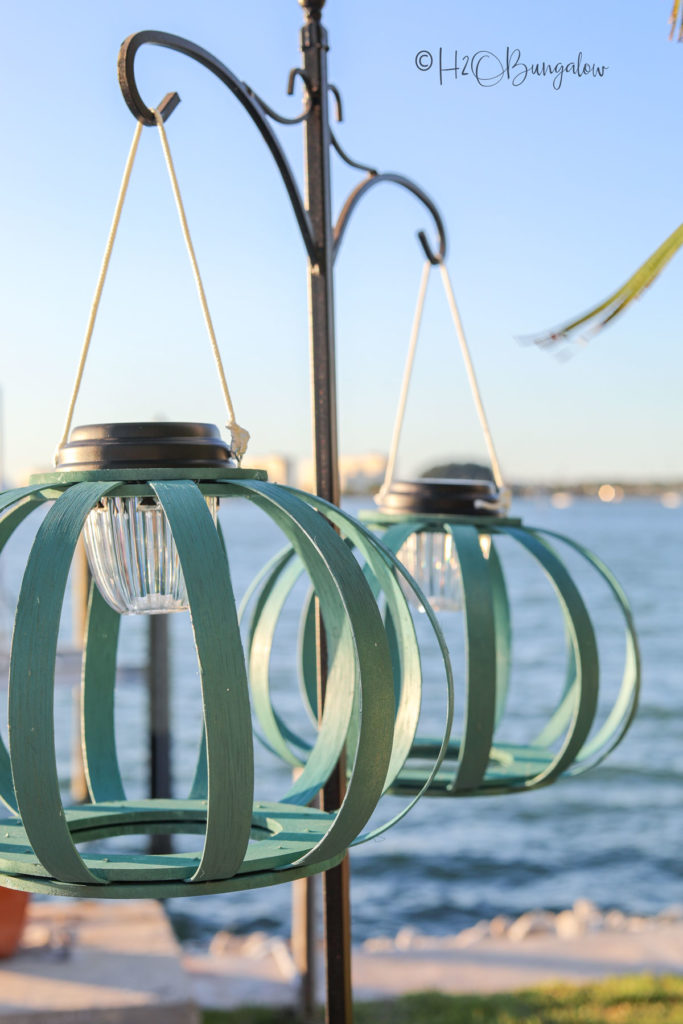 wooden hanging solar lanterns hanging on a pole with the water in the backgournd