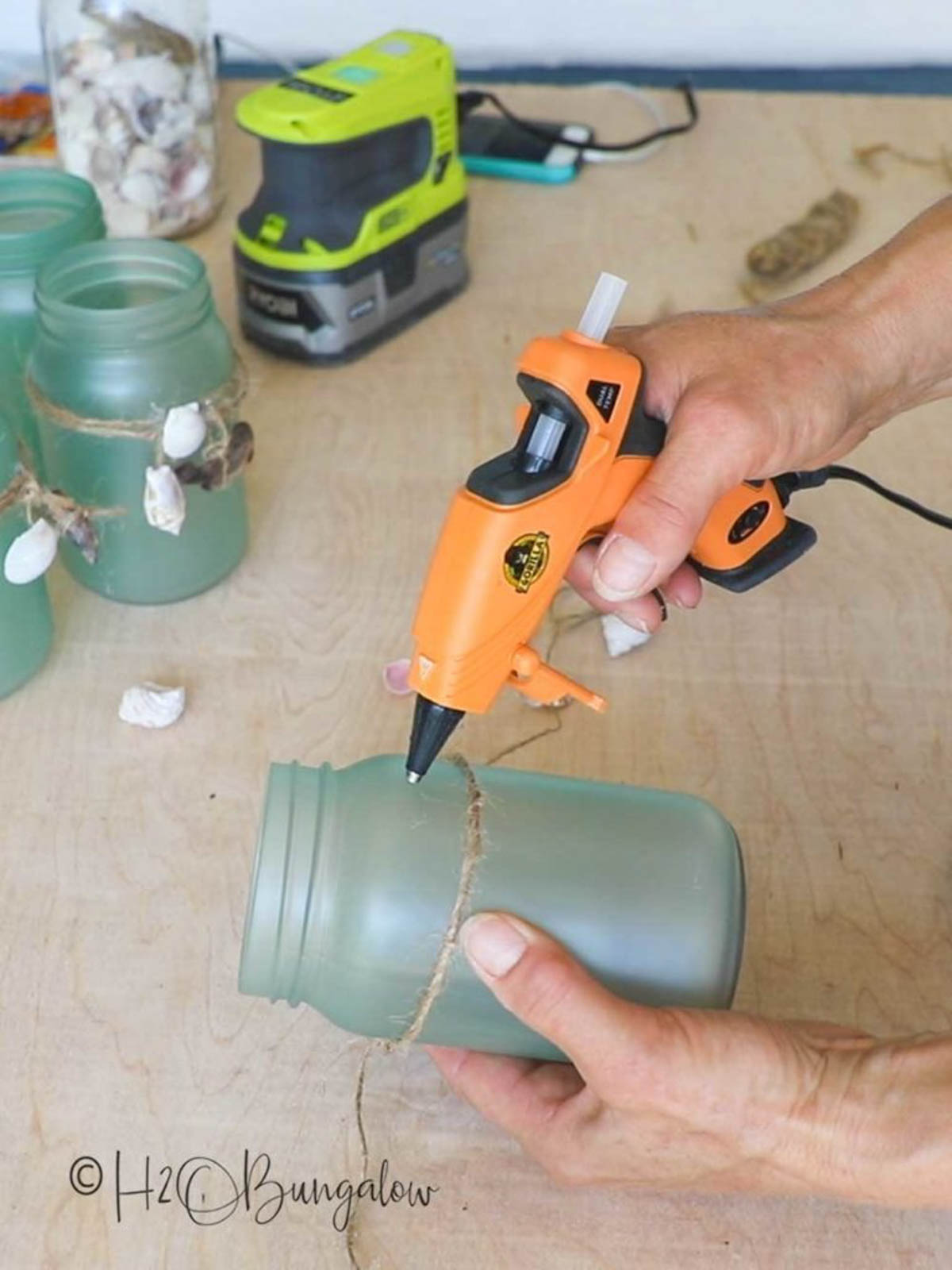 adding twine to glass jar with hot glue for DIY tiki torches