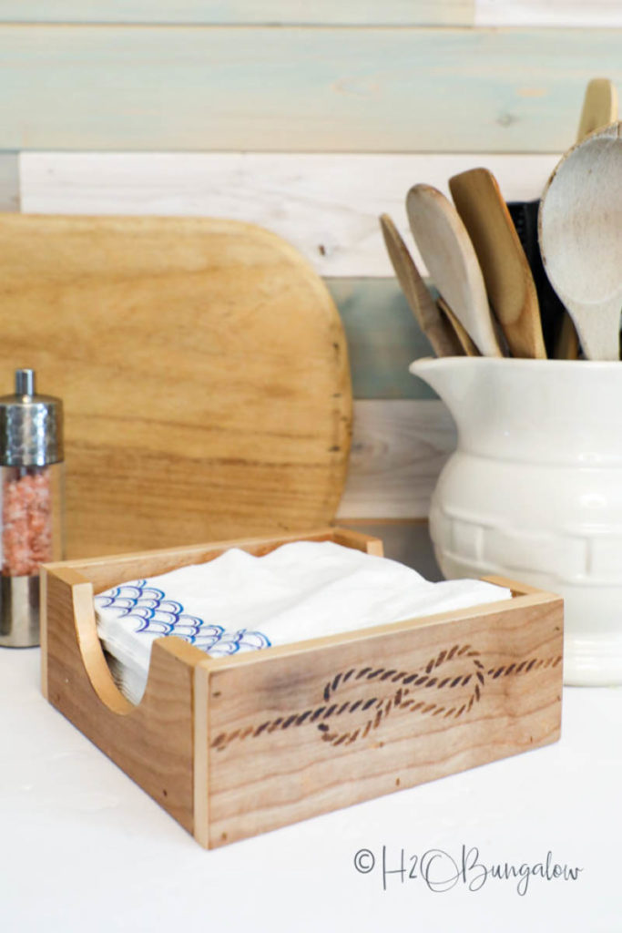 DIY woodworking gift napkin holder made from scrap wood next to cutting board and white pitcher full of of cooking utensils