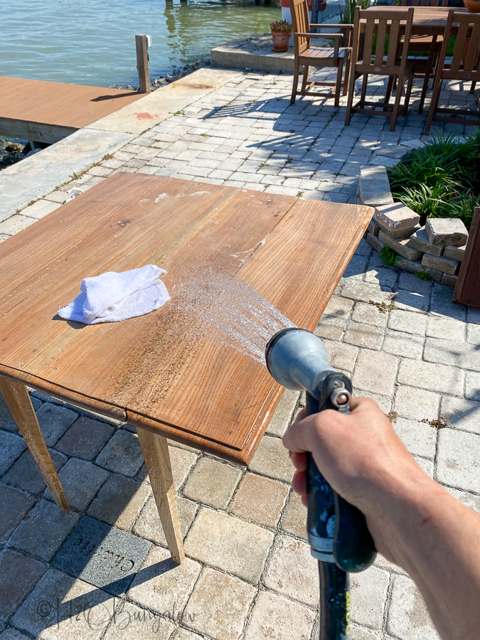 rinsing wood table with a hose to remove bleach residue