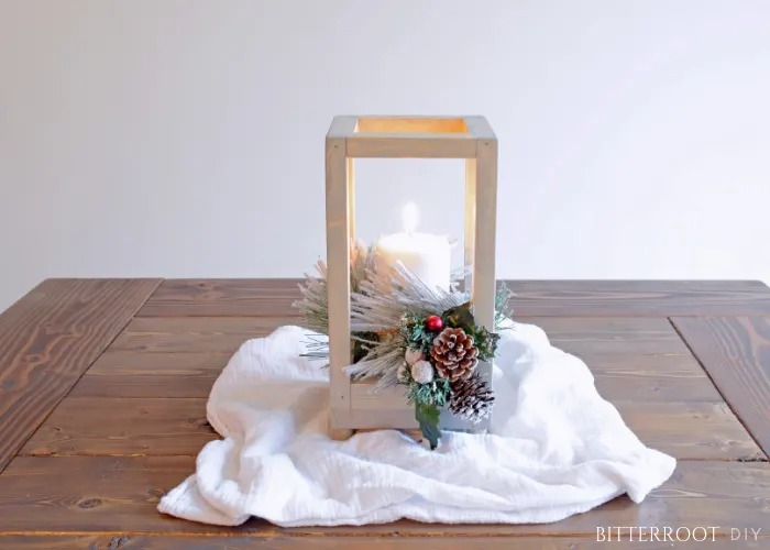 wooden lantern with faux greenery and candle sitting on table